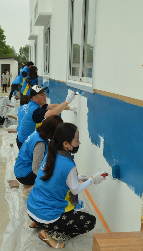 신한은행 봉사단원들이 캄보디아 쩜뻑마을의 교육시설 외벽에 새로 페인트칠을 하고 있다. <사진=신한은행>